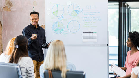 A man shares on the whiteboard in front of his peers.